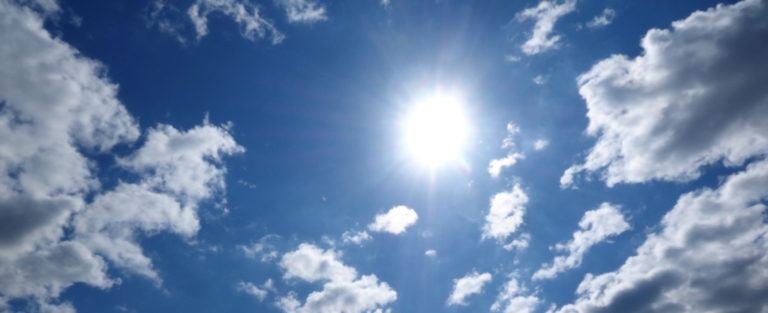 Sonne brennt vom blauen Himmel mit ein paar Wolken