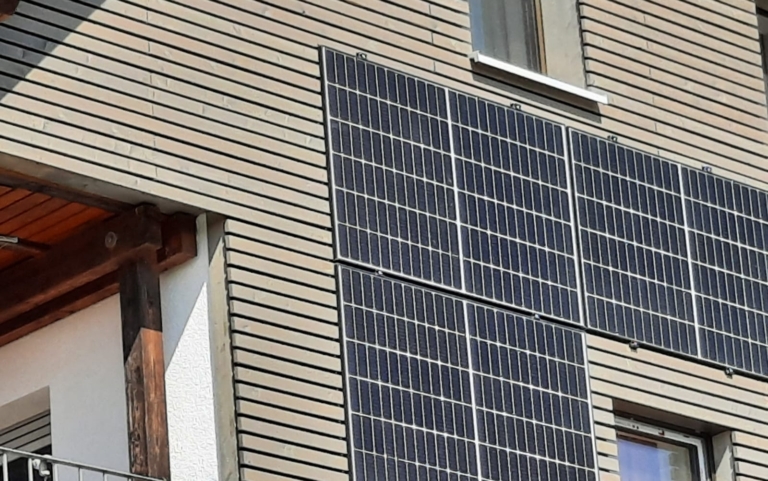 Zwei große Solarpaneele sind vertikal an der Außenwand eines beigen Gebäudes angebracht, direkt unter einem Fenster - und zeigen, wie erneuerbare Energien und Dachsanierung in ein städtisches Wohnumfeld integriert werden können.